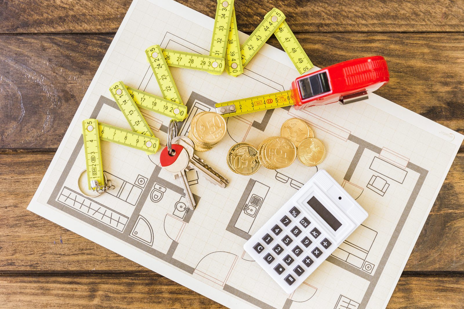 Construction drawings on a desk with a measuring tape, a calculator and stacked coins